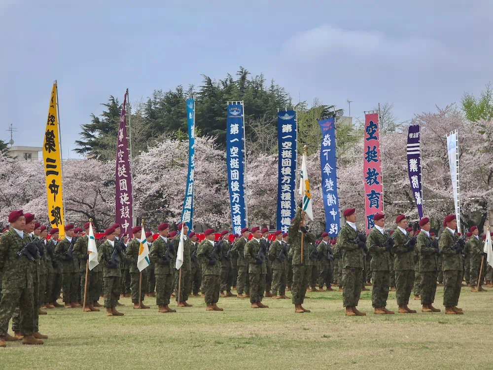 桜を背景に、各部隊の名称が記された色鮮やかな幟（のぼり）と整列する空挺隊員たち