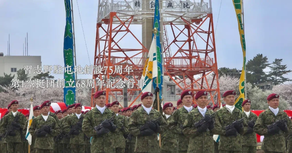 満開の桜と訓練塔を背景に、習志野駐屯地創設75周年・第1空挺団創立68周年記念行事で整列する隊員たち。防衛モニター撮影のアイキャッチ画像