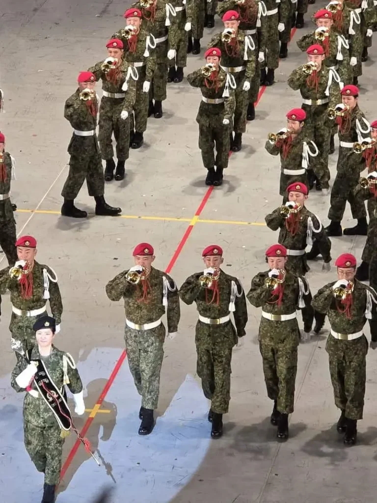 迷彩服姿でらっぱを吹きながら、勇ましく行進する第1師団らっぱ隊の隊員たち（縦位置のショット）