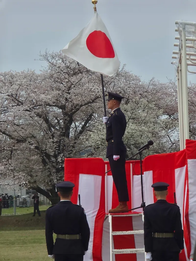 満開の桜を背景に、習志野駐屯地創設75周年・第1空挺団創立68周年記念行事で国旗を掲揚する隊員