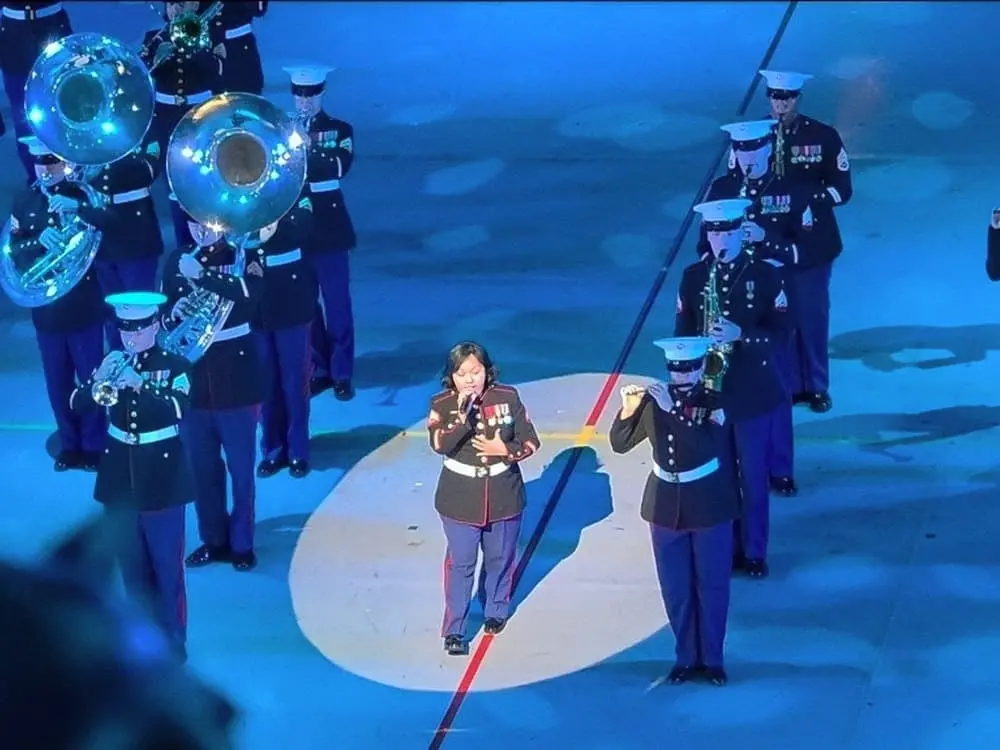 青い照明が輝くステージで、映画『ヘラクレス』の主題歌「Go the Distance」を力強く熱唱する米海兵隊の女性ヴォーカリスト