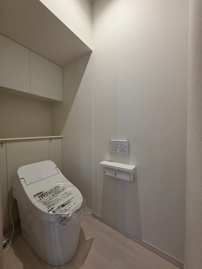 1階トイレ全体の様子（入居前）。タンクレス風トイレ、吊り戸棚、ペーパーホルダーの配置