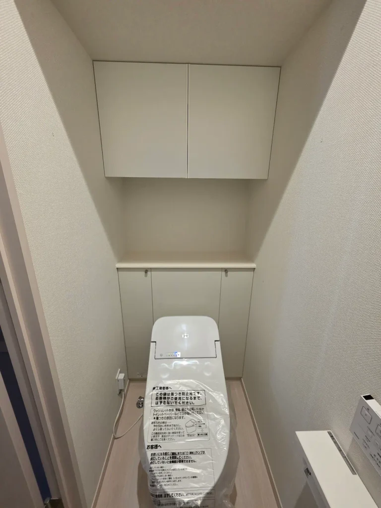 1階トイレの正面写真。タンクレストイレと上部の吊り戸棚収納